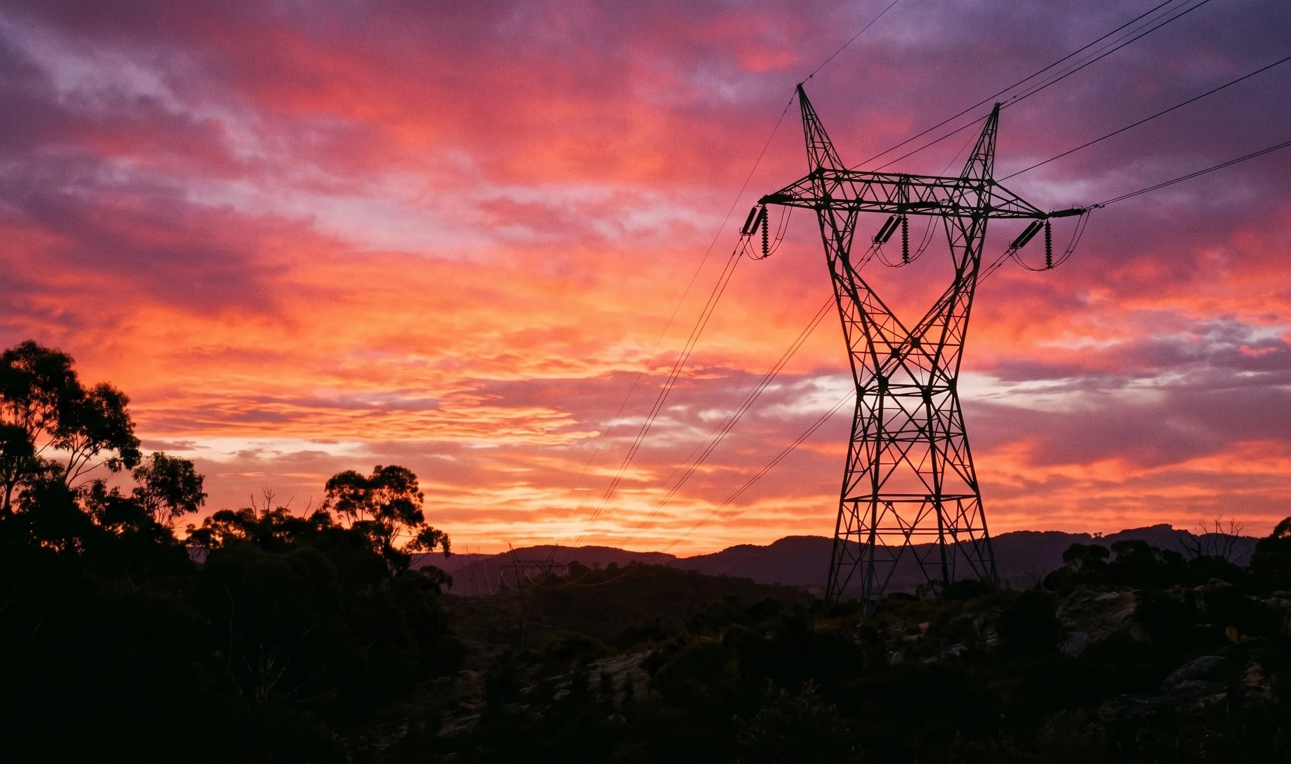 Aerial view of a utility-scale battery storage compound and transmission connection in golden-hour central-west NSW farmland.
